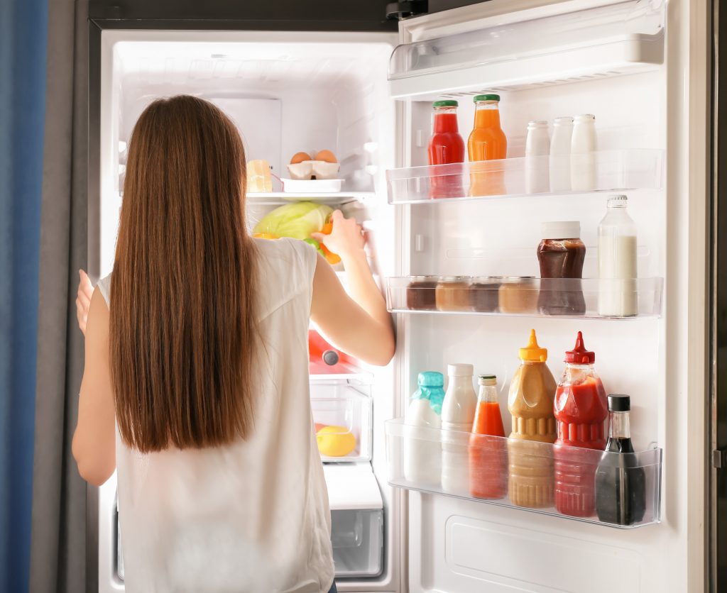 Photo of woman looking at fridge illustrates blog: "How to Store and Reheat Leftover Chicken"