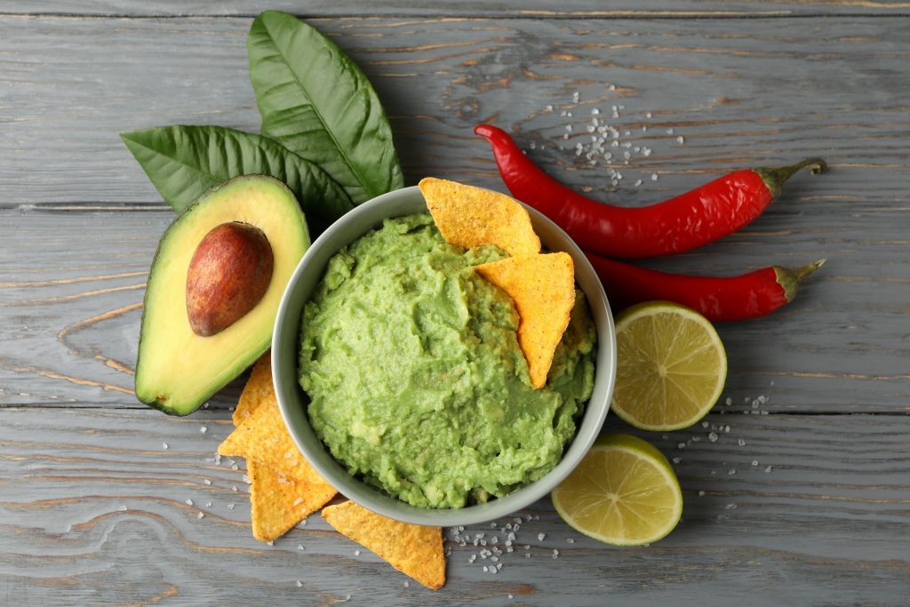 Plate of guacamole with avocados, lime, and chili peppers illustrates blog: "What Do You Eat Guacamole With? 7 Ideas"